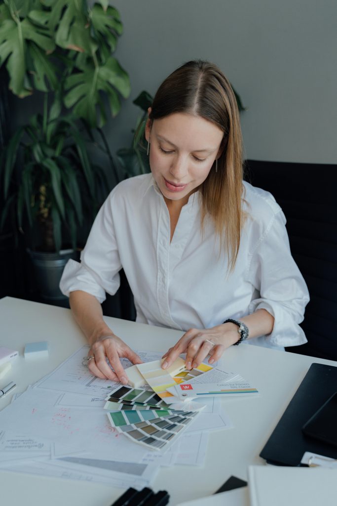 Professional interior designer examining color swatches at desk with plant background, focused and concentrated.